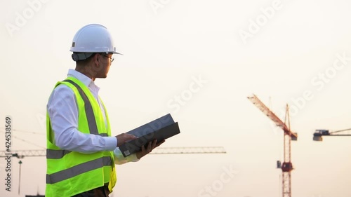 An Asian engineer checking the file with the background of building site at sunset. Media is in slow motion mode.