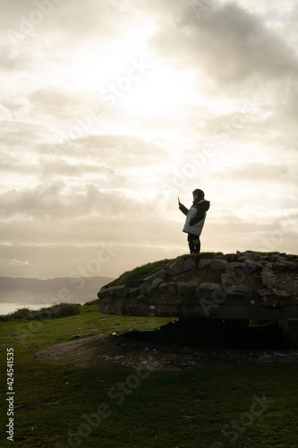 silhouette of a child in a mask looking at a moil phone on a rock