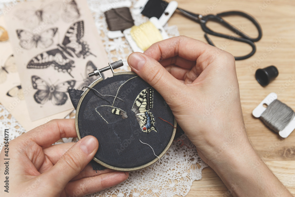 Fototapeta premium Woman embroider a butterfly. Process of making handmade embroidery. Hobby. Sewing tools. Remote home work.
