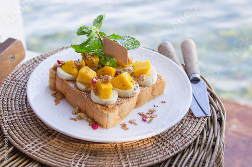 Bread peanut butter in white plate put banana and mango decorated with mint leaves. photo