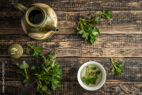 Teapot and cup with nettle tea and nettle leaves on a rustical wooden desk