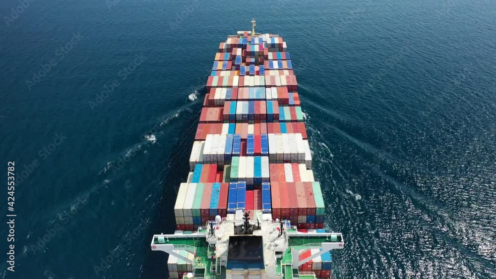 Aerial drone flight above fully loaded container ship cruising open ocean sea for logistics import export, shipping or transportation