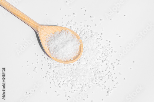 White sea salt on wooden spoon. Isolated on white background. Rustic appearance.