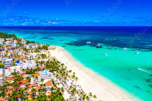 Beach vacation and travel background. Aerial drone view of beautiful atlantic tropical beach with straw umbrellas, palms, boats and pirate ship. Bavaro beach, Punta Cana, Dominican Republic.