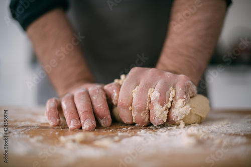 A male chef prepares noodle dough at home in the kitchen. Close up of hands with flour and dough