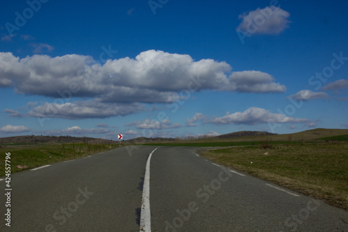 Asphalt road with a white dividing strip going beyond the horizon. Blue sky with fluffy white clouds