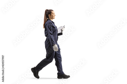 Full length portrait of a female worker in a uniform walking and holding a clipboard