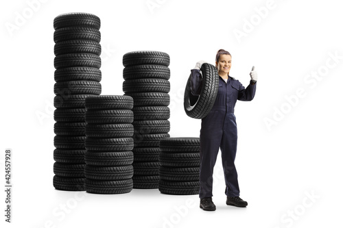 Full length portrait of a female mechanic with piles of tires showing thumbs up photo