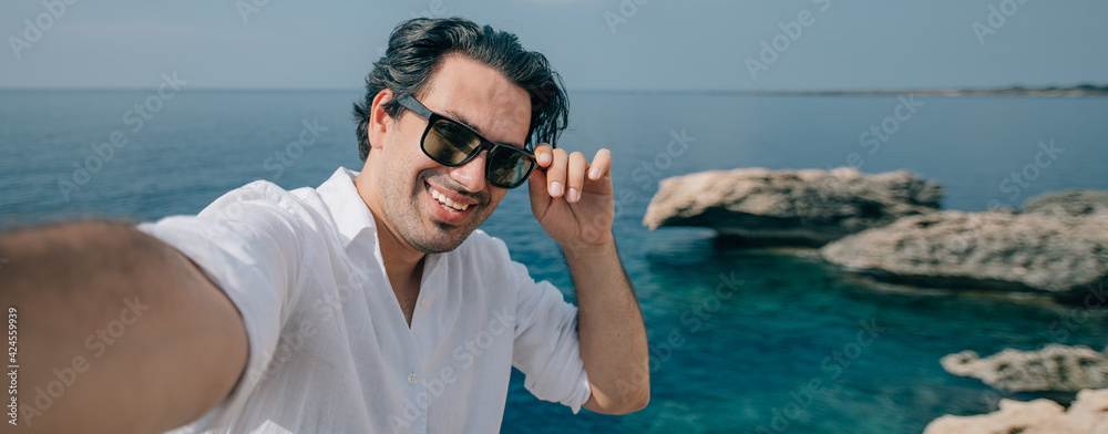 A man takes a selfie on the rocks with a sea view