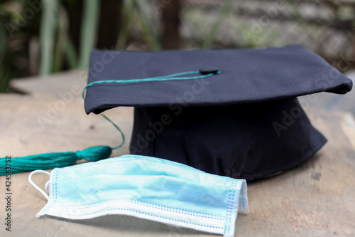 Black graduation cap with blue tassel standing on a background with medical mask. Horizontal image
