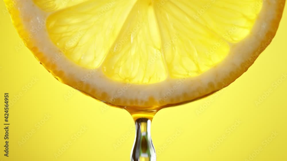Super Slow Motion Macro Shot of Water Drop Falling from Lemon Slice on Yellow Background at 1000fps.
