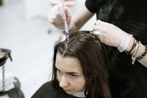 process of coloring the hair and painting over the gray hair of a young woman in a beauty salon