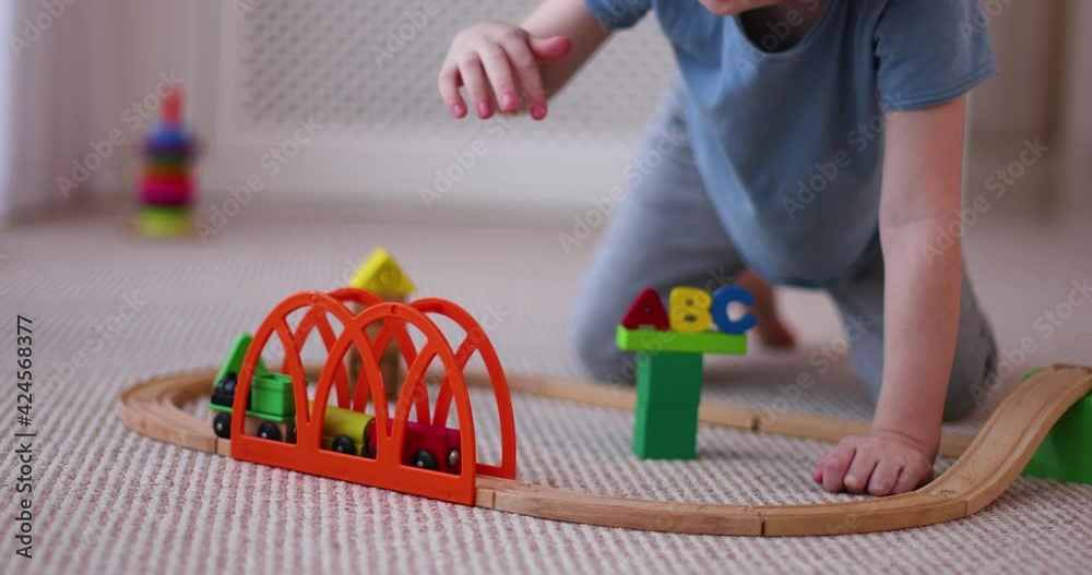 happy kid playing with wooden train on toy railway road at home