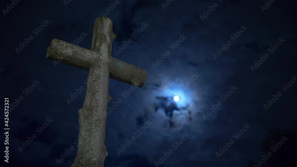 Stone tomb cross in the cemetery at night with a cloudy full moon. Handheld shot. Stone tomb cross in the cemetery at night with a cloudy full moon. Handheld shot.