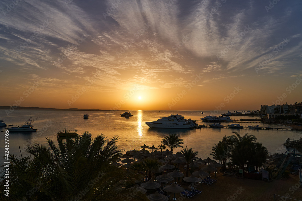 Delightful sunrise at sea with palm trees and yachts in the background. Tourism concept