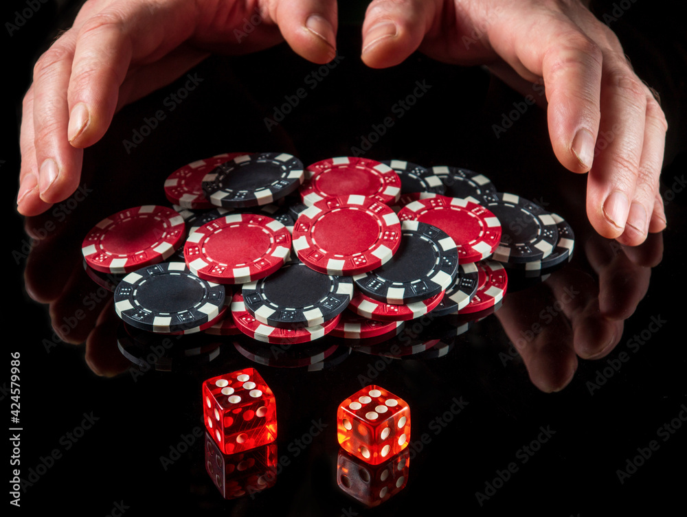 Dice with the maximum winning combination of twelve in poker on a black table and chips with hands in the background