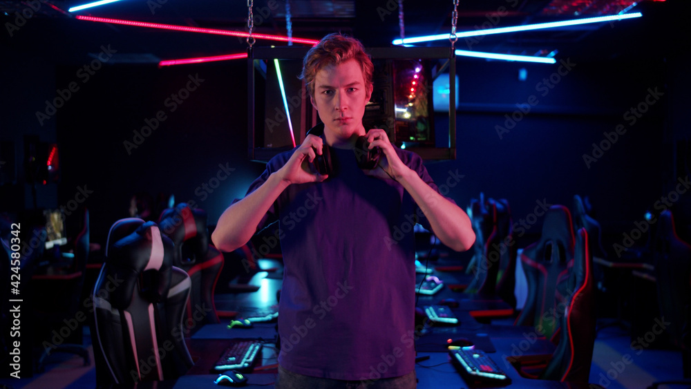 © iaginzburg - Cute guy gamer in a blue T-shirt in the computer room puts on a headset, then takes it off