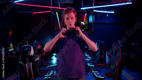 Cute guy gamer in a blue T-shirt in the computer room puts on a headset, then takes it off