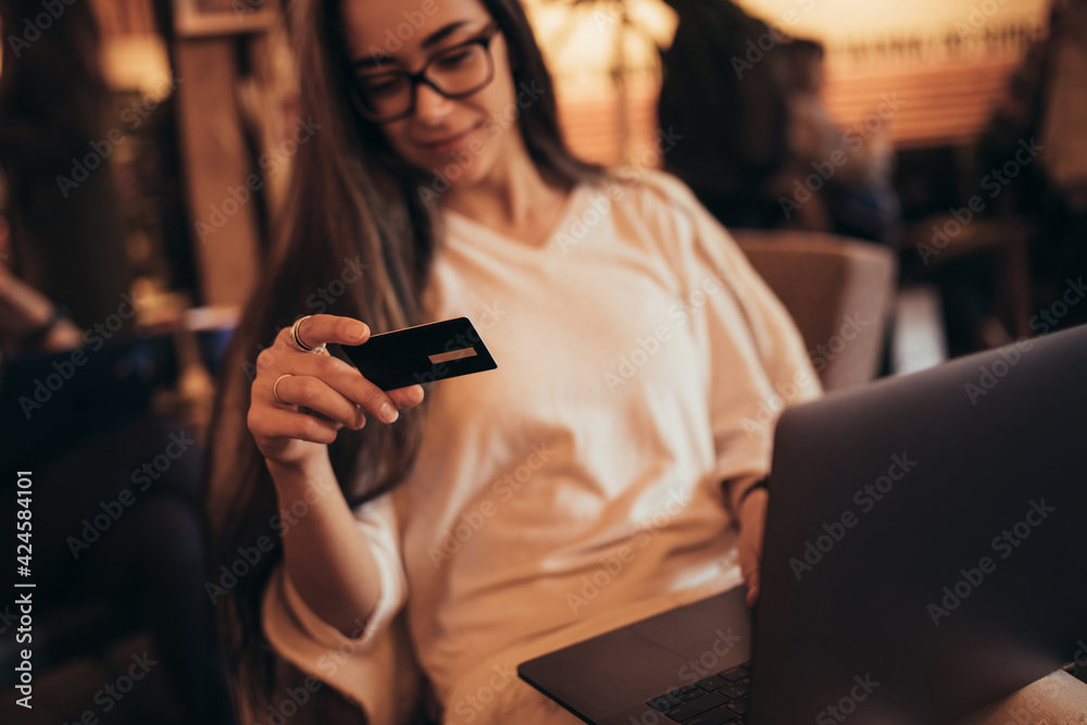Young woman millennial sitting in a coffee shop and shopping online using her laptop and credit card.
