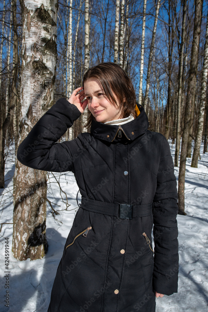 Beautiful woman in black coat smiling in a snowy birch forest Beautiful woman in black coat smiling in a snowy birch forest