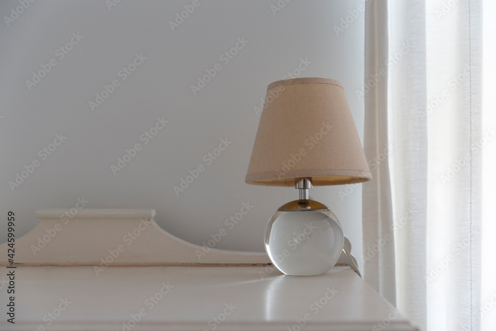 Close up of a small lamp standing on wooden decorative table next to the curtain.