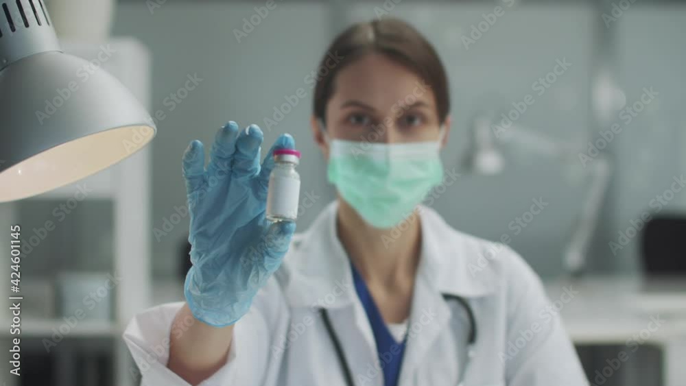 Close-up of a bottle with a vaccine or medicine in the hands of a young female doctor Close-up of a bottle with a vaccine or medicine in the hands of a young female doctor