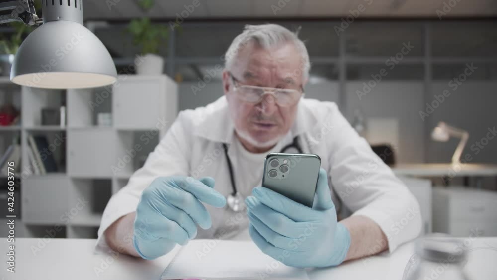 A doctor during a heavy shift in an infectious diseases hospital talks to relatives on a video call via a smartphone. Interior of the medical office. A doctor during a heavy shift in an infectious diseases hospital talks to relatives on a video call via a smartphone. Interior of the medical office.