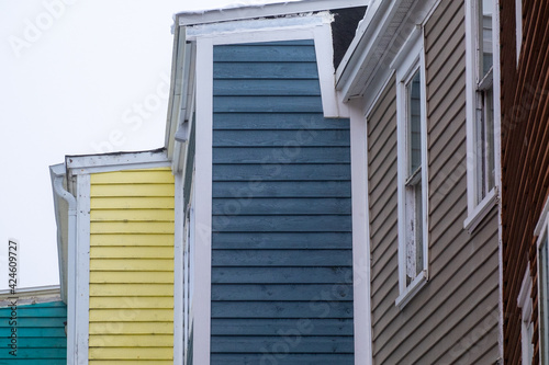 The top corners of five wooden buildings or houses in a step formation. All the buildings have bright coloured wood horizontal clapboard siding with double hung windows and white trim under a grey sky