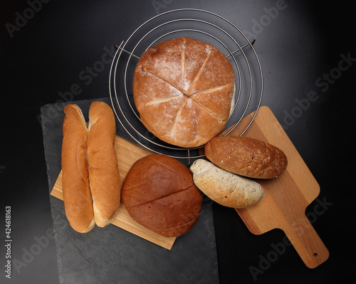 Freshly baked bread loaf bun roll round long mix verity on wooden board metal grill over black background photo