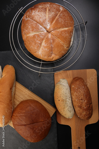 Freshly baked bread loaf bun roll round long mix verity on wooden board metal grill over black background photo