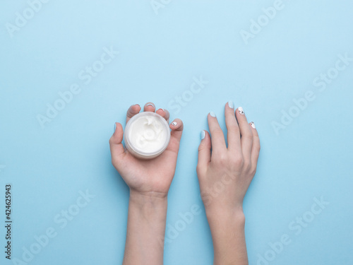 Fototapeta Naklejka Na Ścianę i Meble -  Women's hands with a jar of hand cream on a blue background. Flat lay.