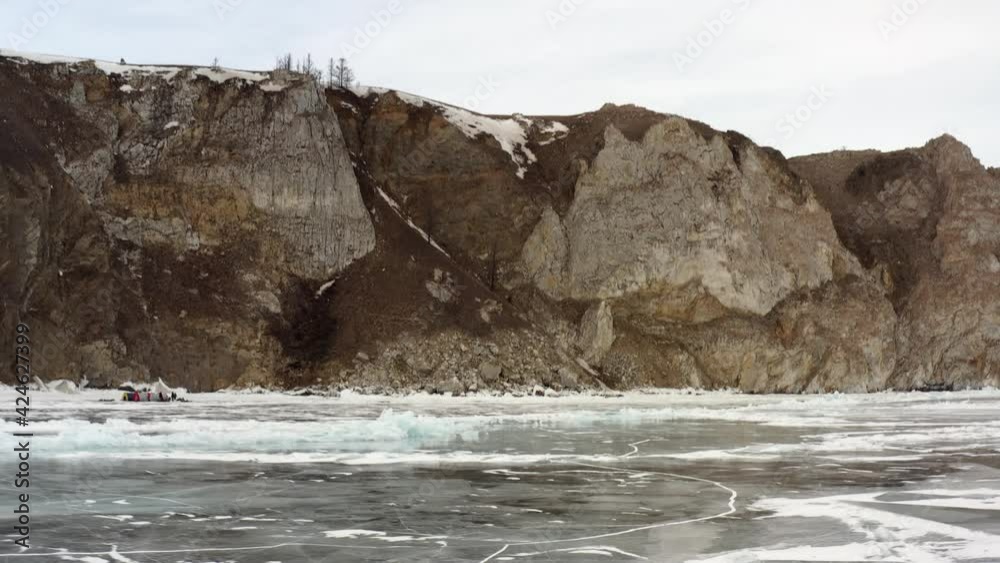 Fly directly on a drone on frozen Lake Baikal, close to the rocky coast