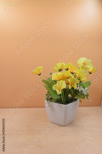 flor amarilla en florero blanco, sobre superficie de madera y fondo naranja. en posición vertical y alineada a la derecha