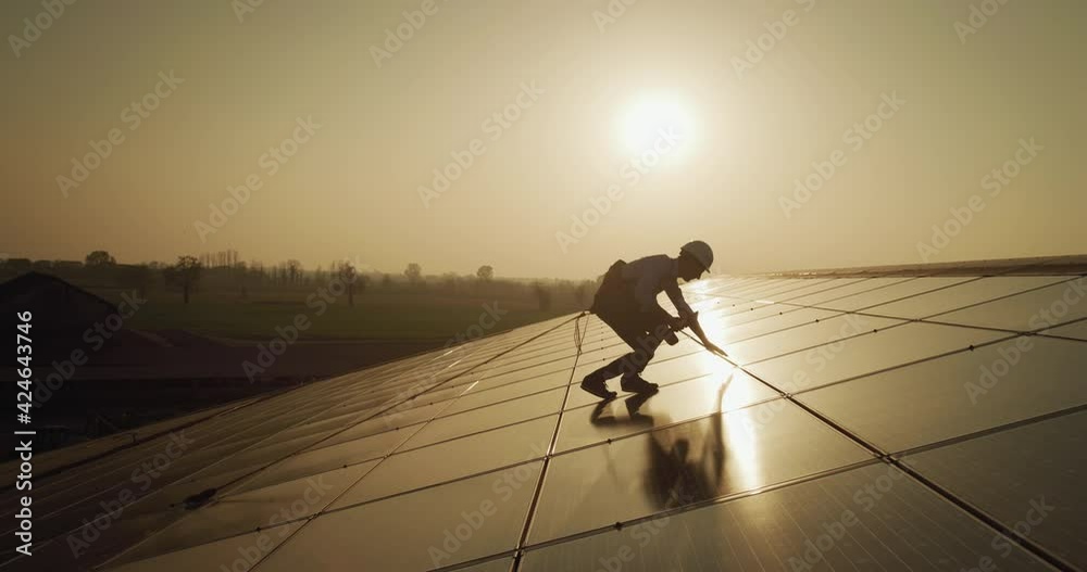 Cinematic shot of assistance technical worker in uniform checking operation and efficiency of photovoltaic solar panels on roof at sunset. Concept: sustainable renewable green, bio eco clean energy.