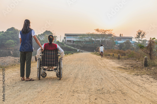 Rear view of disabled handicapped woman in wheelchair and care helper walking in park.