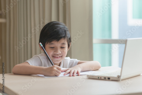 Little Asian child using a pencil to write on notebook at the desk,Social Distance,E-learning online education