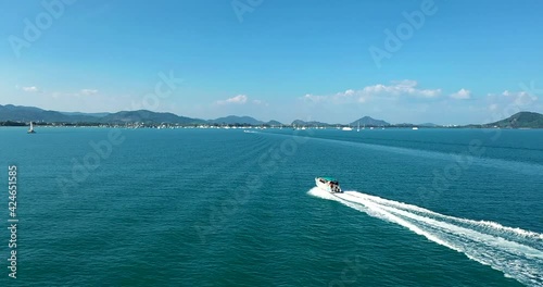 Aerial View sideways motorboat tropical. Aerial view: fast moving speed boat wake on clear blue sea water, turquoise building, ship shore, waves, green forest