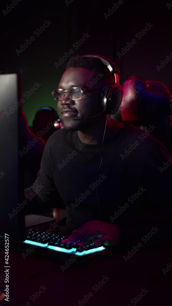 A kind dark-skinned guy plays a video game on the computer, he talks to his teammates on teamspeak A kind dark-skinned guy plays a video game on the computer, he talks to his teammates on teamspeak