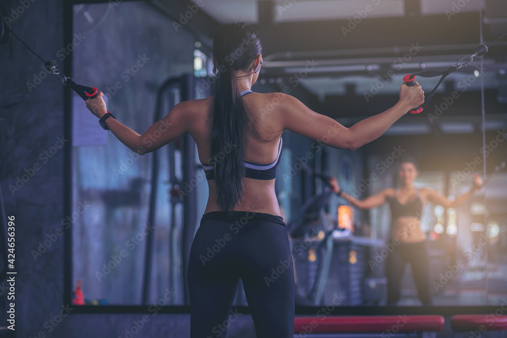 Fototapeta premium Happiness woman exercise with cable weight machine in front of mirror at fitness gym. Selected focus