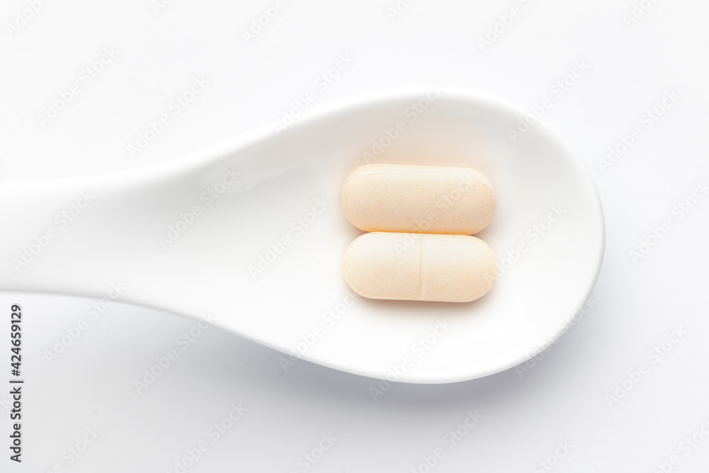 Macro Close up of medicinal or herbal pale yellow tablet on a white ceramic spoon. Top view, white background. Macro Close up of medicinal or herbal pale yellow tablet on a white ceramic spoon. Top view, white background.