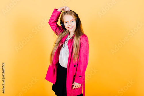 Portrait of happy girl in raincoat and boots standing on yellow background