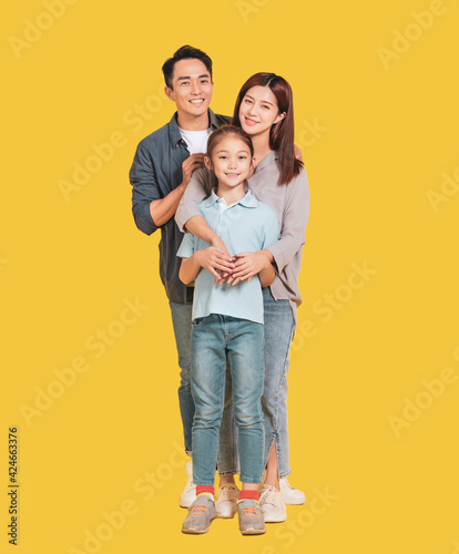 Happy Asian young family with one child standing embracing and smiling at camera isolated on yellow © Tom Wang