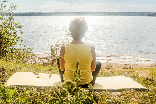 Senior woman meditate near river, back view. photo