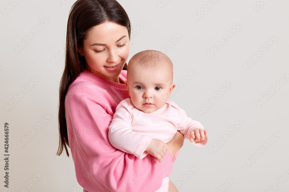 Dark haired Caucasian mother with long dark hair holding her cute baby girl wearing bodysuit, woman in casual outfit looking at her daughter with love, isolated over white background. Dark haired Caucasian mother with long dark hair holding her cute baby girl wearing bodysuit, woman in casual outfit looking at her daughter with love, isolated over white background.