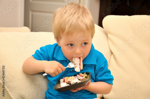 Adorable boy eating cake in a chair with a fork