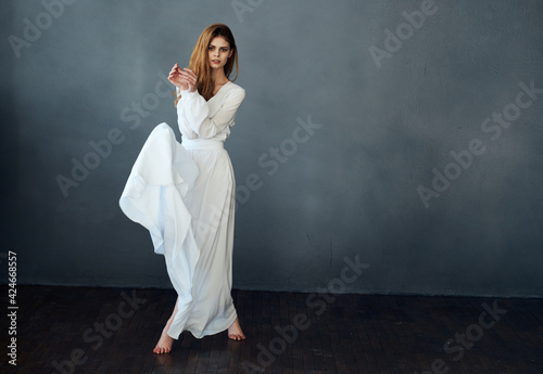 A romantic woman in a white dress in full growth is dancing on a gray background