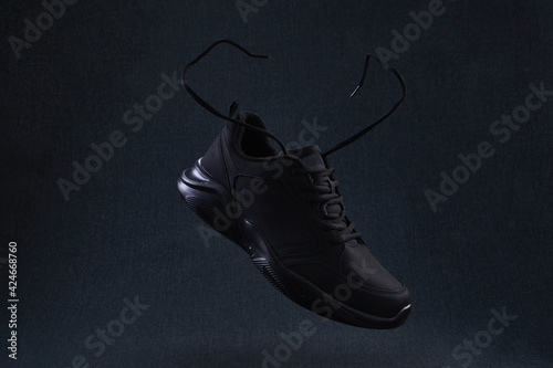 Fashion black unbranded sneaker with laces flying on dark background. Black sport running shoes levitate in air.