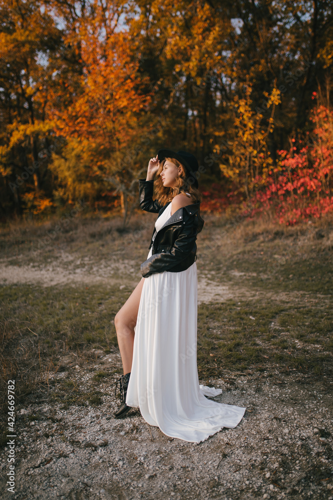 Beautiful young bride wearing stylish wedding dress with black hat and jacket in autumn forest.
