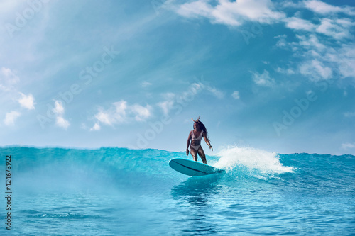 Charming curly African-American dark-skinned young woman, professional surfer do noseride on a long surfboard 