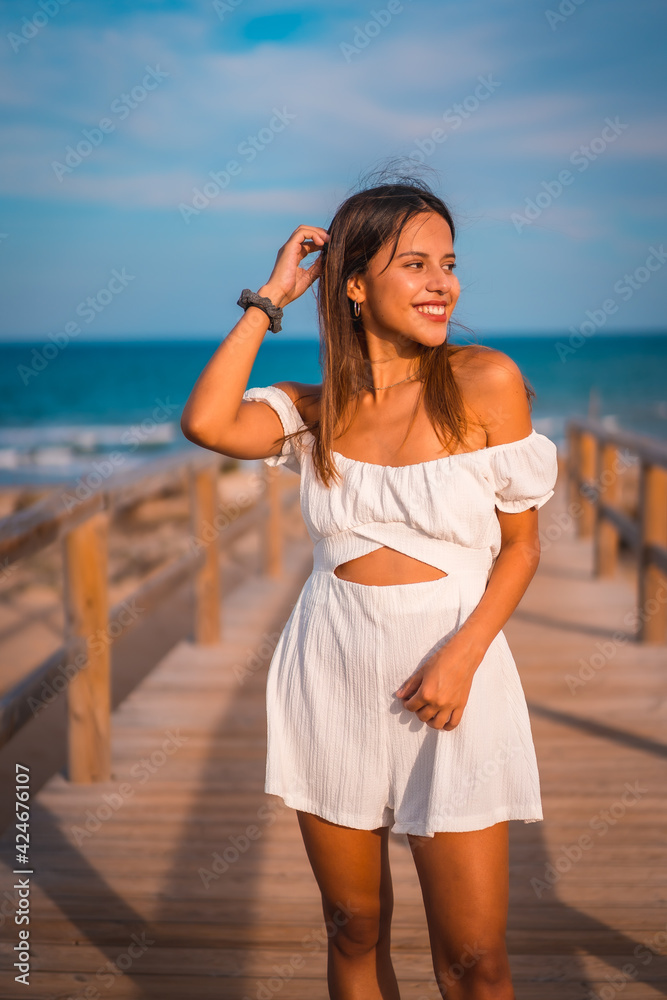 Lifestyle of a young brunette Caucasian on vacation on the beach wearing a white dress in summer, walking along the wooden walkway Lifestyle of a young brunette Caucasian on vacation on the beach wearing a white dress in summer, walking along the wooden walkway